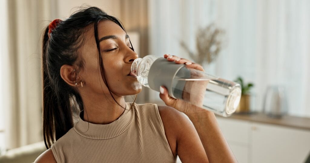 Woman drinking water after searching how long does it take to detox from drugs.